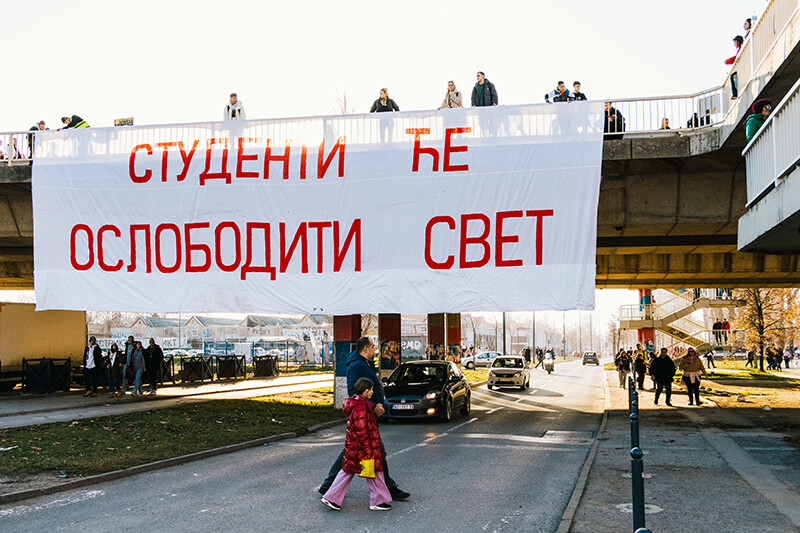 Veliki transparent iznad ulice i ljudi na nadvožnjaku tokom studentskog protesta.
